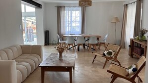 A spacious living room with a sofa, a coffee table, and a dining area with chairs. - Charming house (Travaillan)