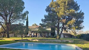 A rectangular swimming pool surrounded by grass, with trees and a building in the background. - Charming house (Travaillan)