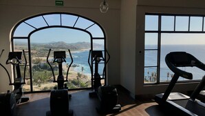 A gym with exercise equipment and a large arched window overlooking a coastal landscape. - 3-bedroom, 5-bathroom Luxury Villa at the Residences in Hacienda Encantada (Cabo San Lucas)