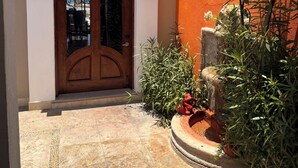 A building entrance with a wooden door, two wall-mounted lanterns, and a small garden with plants and flowers. - 3-bedroom, 5-bathroom Luxury Villa at the Residences in Hacienda Encantada (Cabo San Lucas)