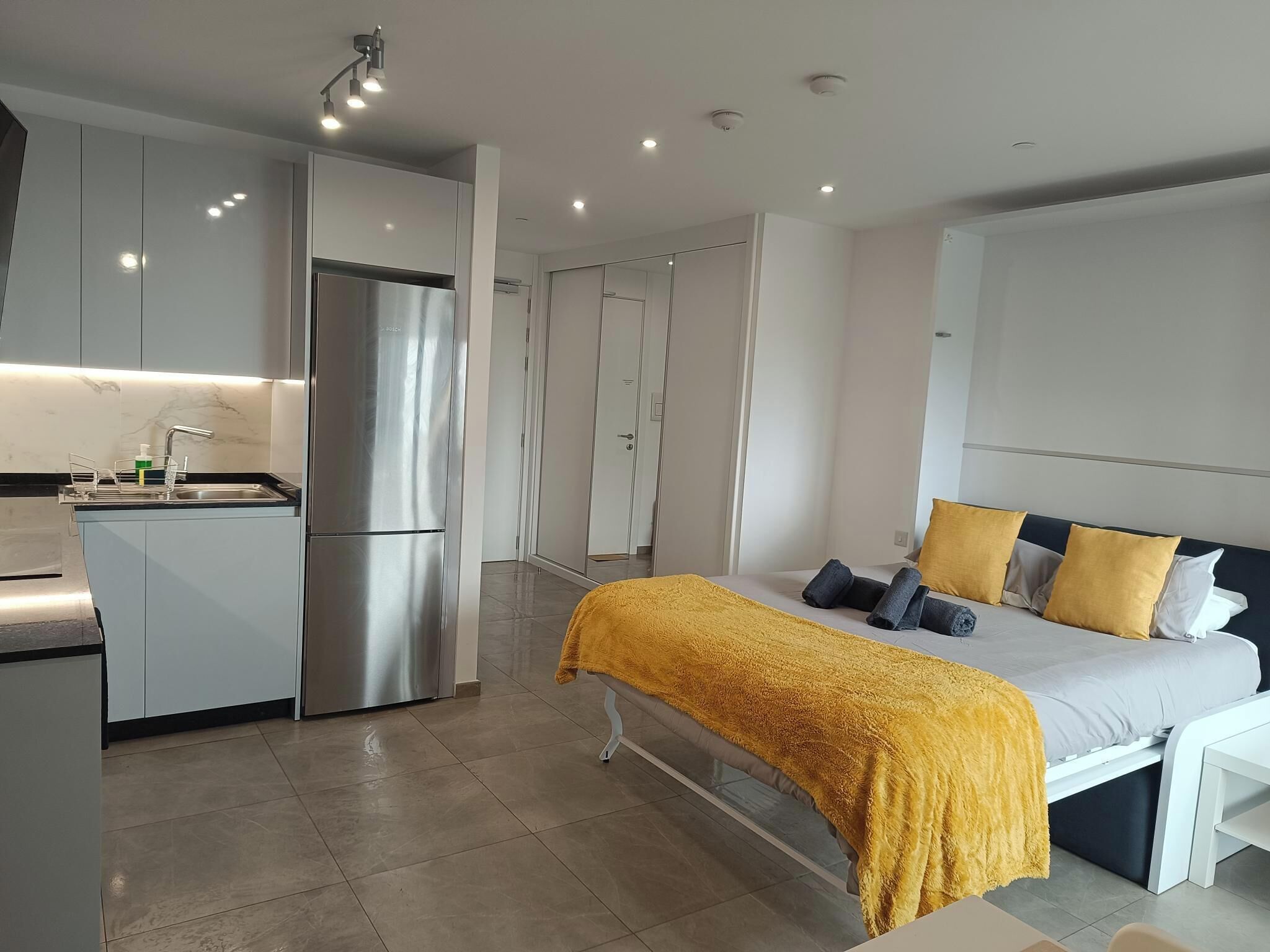 Una habitación de hotel moderna con una cama, una mesita de noche y una zona de kitchenette.