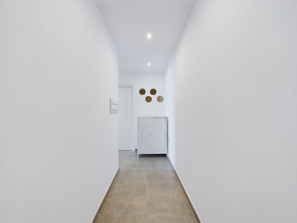 A narrow, white-walled hallway with a tiled floor, leading to a door with circular wall decorations above it. - E1 18th Floor Studios - Scenic Sea & Beach Views (Gibraltar)