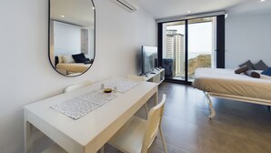 A modern hotel room with a bed, a desk, a chair, a TV, and a large window offering a city view. - E1 18th Floor Studios - Scenic Sea & Beach Views (Gibraltar)