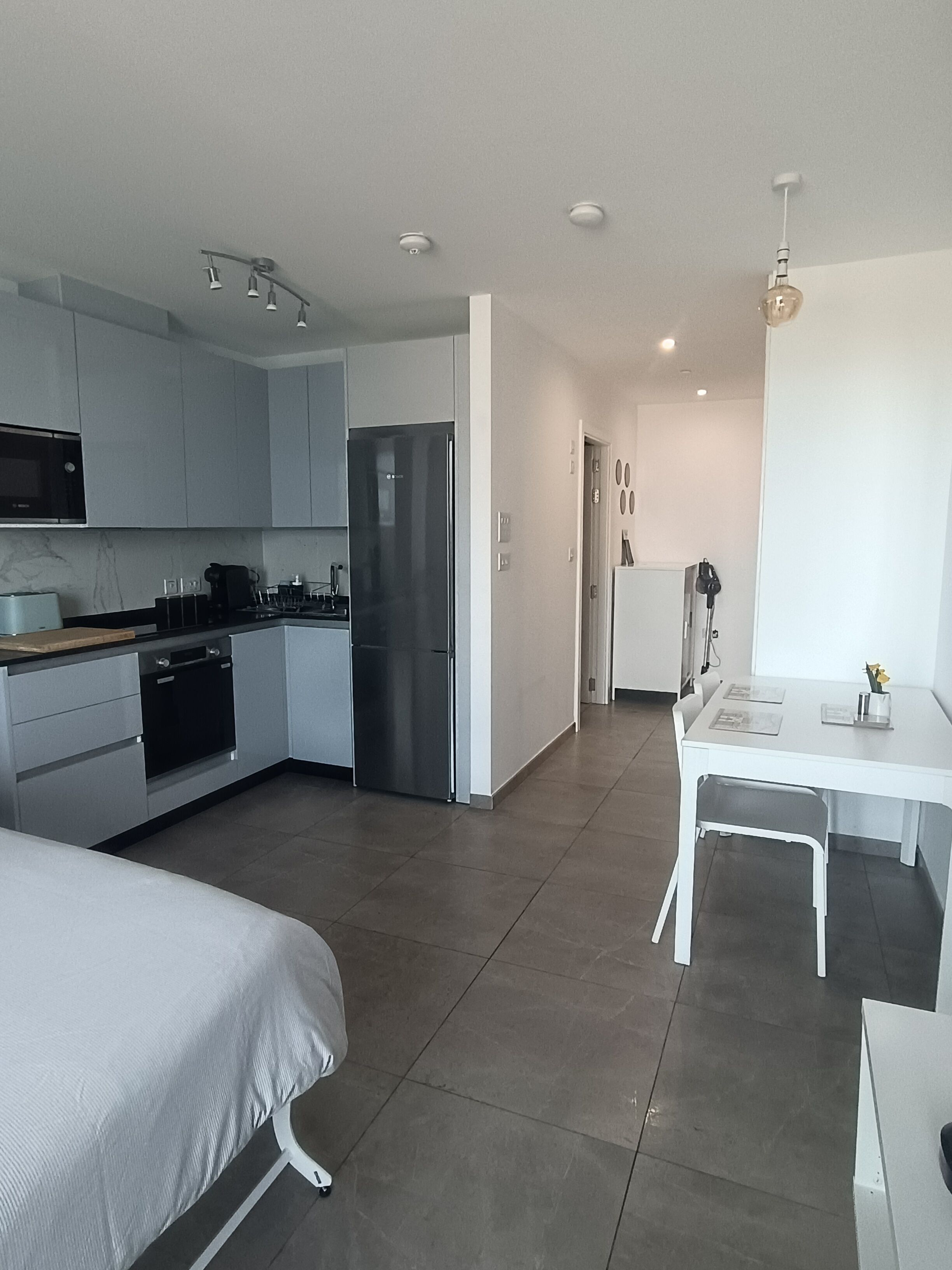 A modern kitchen with grey cabinets, a stainless steel refrigerator, and a dining area with a white table and chairs.