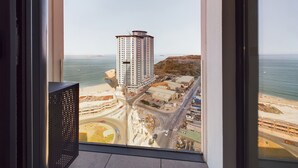 Um edifício alto com vista para a paisagem costeira, incluindo uma praia e uma autoestrada.