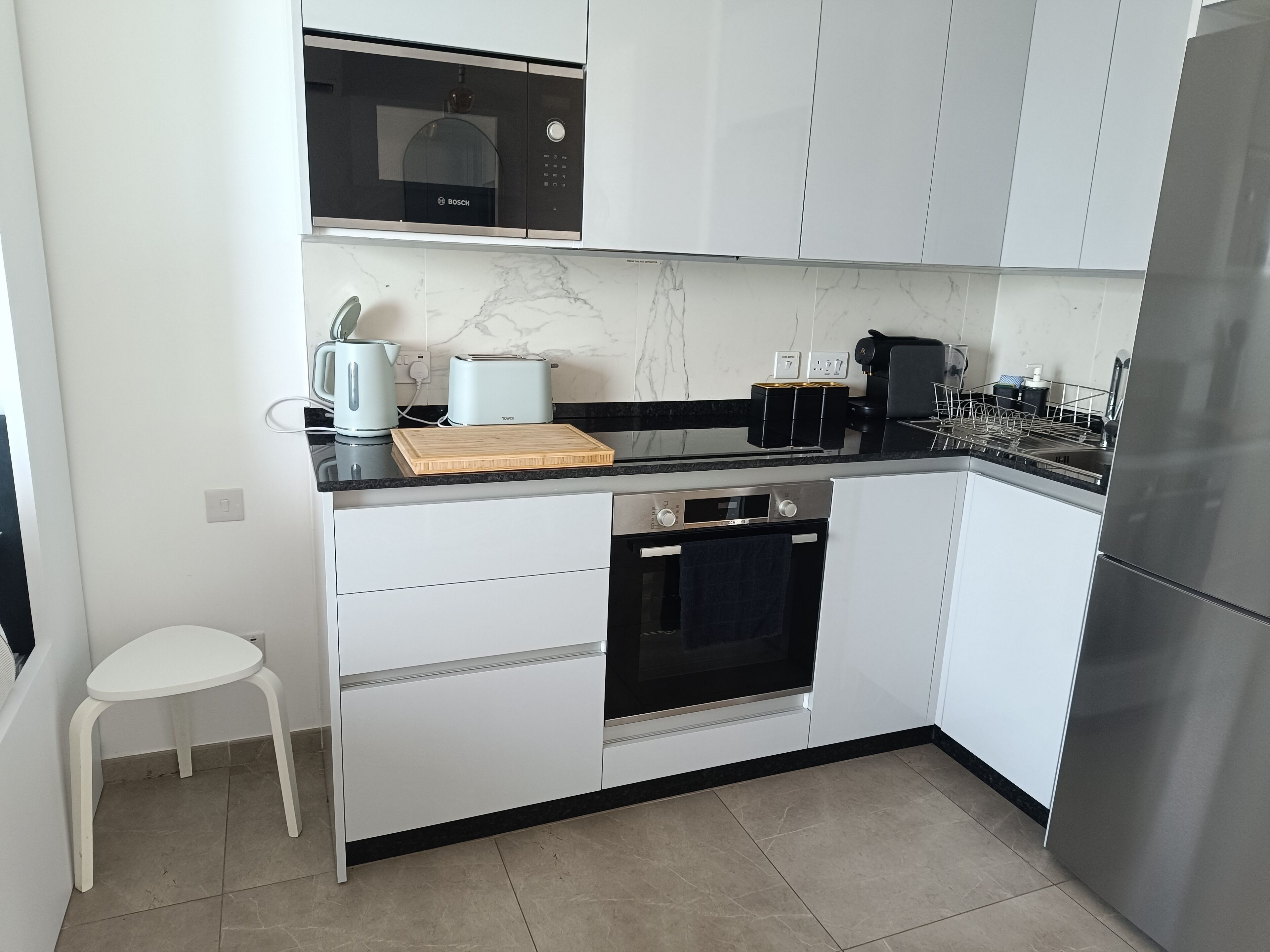 A modern kitchen with white cabinets, a Bosch microwave, a toaster, and a stainless steel refrigerator.