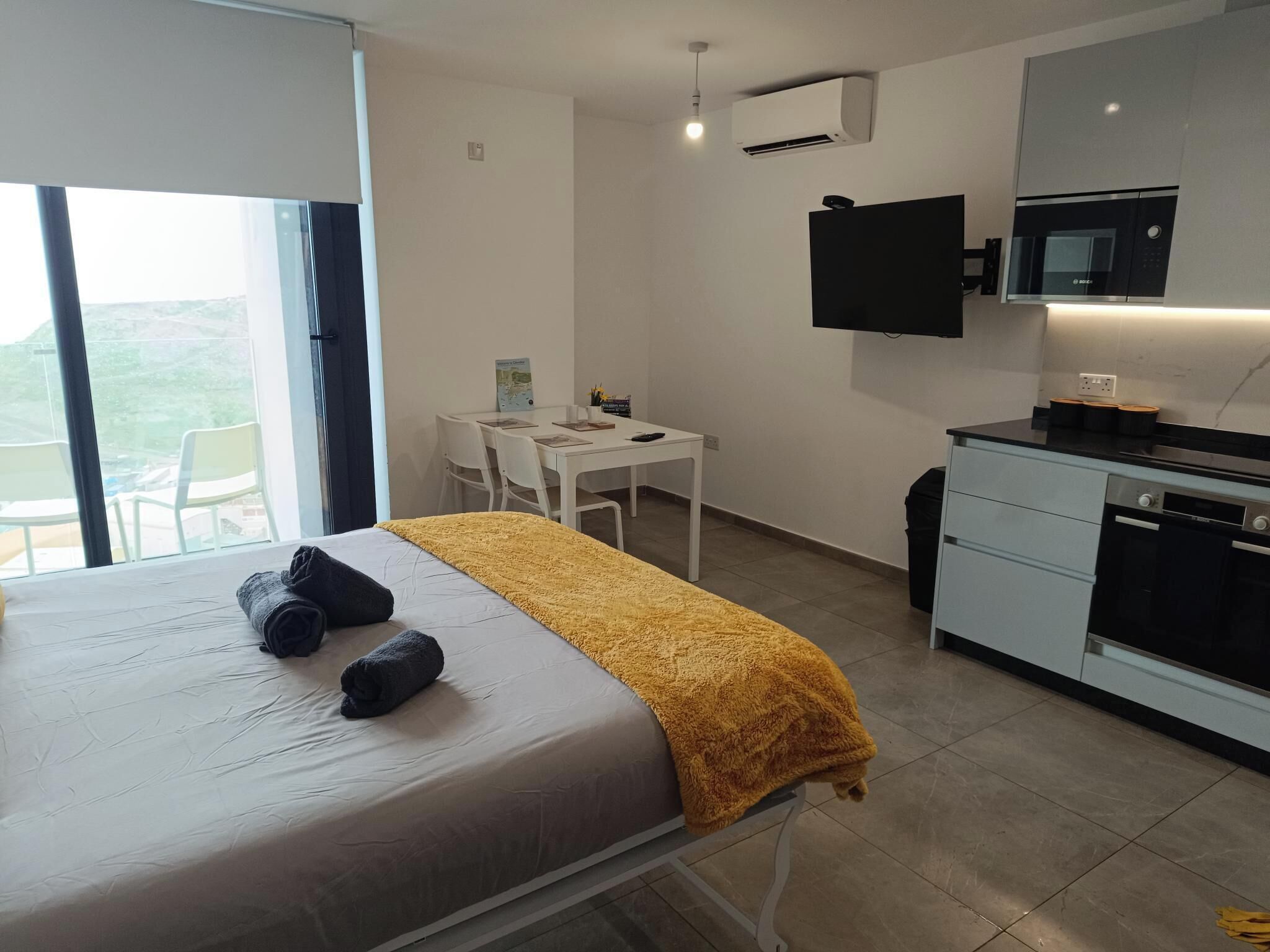 Una habitación de hotel moderna con una cama, un escritorio pequeño, un televisor de pantalla plana y una kitchenette.