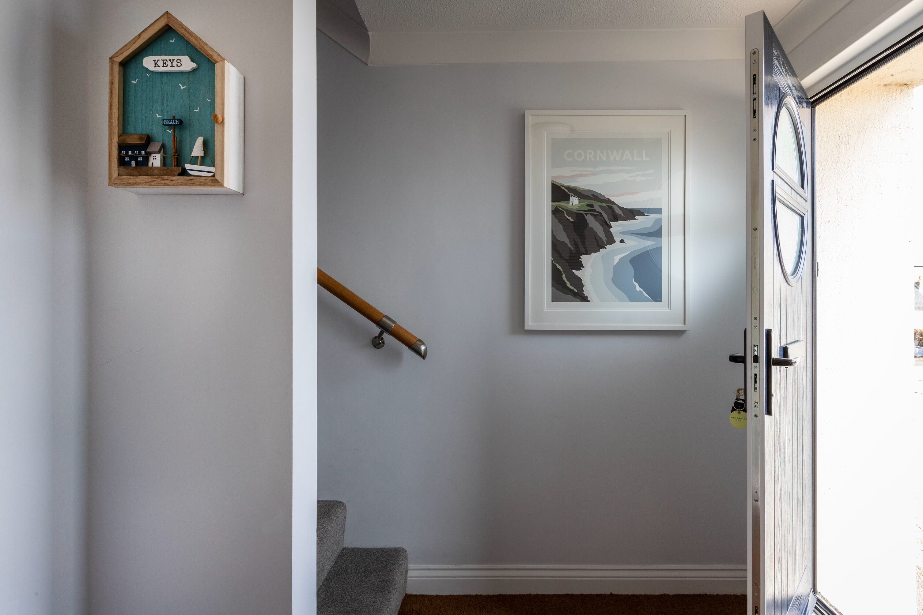 A hallway with a wooden key display, a framed picture of a coastal scene, and a door with a key in the lock.