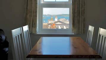 A dining table with four chairs, a window with curtains, and a view of buildings and water.