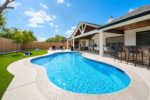 Une piscine à bords incurvés, entourée d’un patio aménagé avec des chaises et un bar.