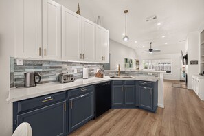 Una cocina moderna con armarios blancos y azul marino, un protector contra salpicaduras de piedra e isla central con fregadero.