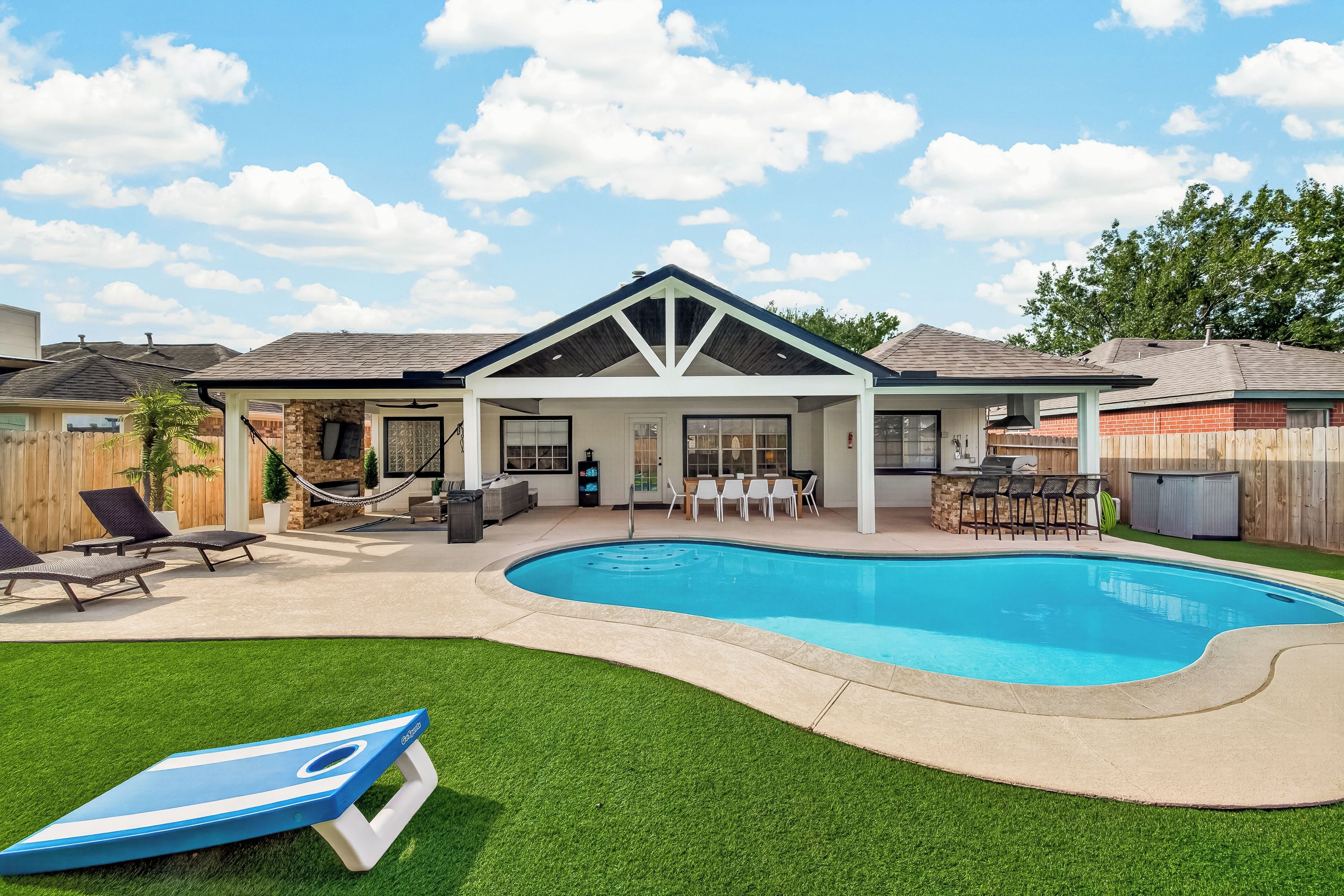 Un patio trasero con piscina, terraza techada y césped.