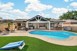 Un patio trasero con piscina, terraza techada y césped.