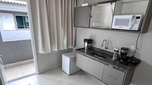 Una cocina compacta con microondas, cafetera y refrigerador pequeño.
