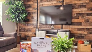 Una sala de estar con pared de madera, televisor de pantalla plana, sofá, mesa de centro con libros y una planta, y chimenea.