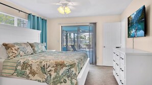 A bedroom with a bed, a ceiling fan, a TV, and a sliding glass door leading to a balcony.