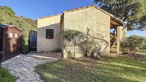 A rustic house with a stone pathway leading to a wooden door, surrounded by greenery and a clear blue sky.