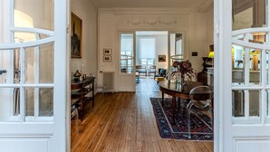 A spacious room with wooden flooring, a dining table with chairs, and a view of a living area through an open door.