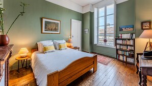 A bedroom with a wooden bed, a bookshelf, a window with a view, and a door.