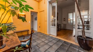 A room with a tiled floor, a wooden table, a chair, a potted plant, and a door leading to another room.