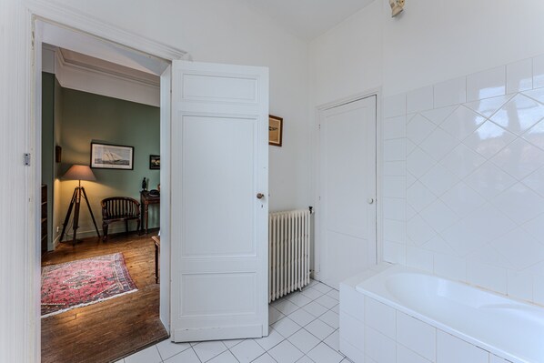 A bathroom with a white bathtub, a radiator, and a door leading to another room.