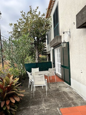 Relax in the patio area with a table and two chairs, surrounded by a lush tree and a green fence.