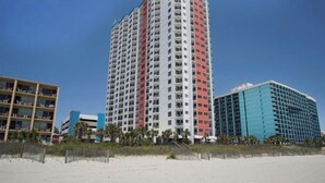 A tall, multi-story hotel with a distinctive red and white facade, located near a beach. - Ocean View Palace Resort 1813- 2BR- Pool, Hot Tub (Myrtle Beach)