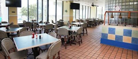 A spacious indoor dining area with multiple tables and chairs, large windows, and ceiling fans.
