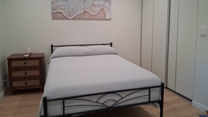 A bedroom with a bed, a nightstand, a wardrobe, and a wall art piece.