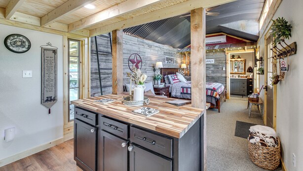 A kitchen with wooden cabinets, a central island, and a dining area with a table and chairs. - Cozy Retreat w/ Ponds, Kayaks & Fire Pit (Okolona)