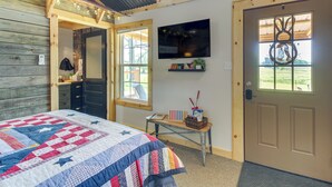 A bedroom with a large bed, a TV mounted on the wall, and a door with a decorative window. - Cozy Retreat w/ Ponds, Kayaks & Fire Pit (Okolona)