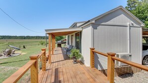 A wooden deck leading to a building with a covered porch, outdoor seating, and a view of a green field. - Cozy Retreat w/ Ponds, Kayaks & Fire Pit (Okolona)