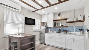 A modern kitchen with white cabinets, a wooden dining table, and a built-in TV. - Sala Suite 1! Monday & Thursday Fall Promo! Pet Friendly, Walk to Beach! (St. Pete Beach)