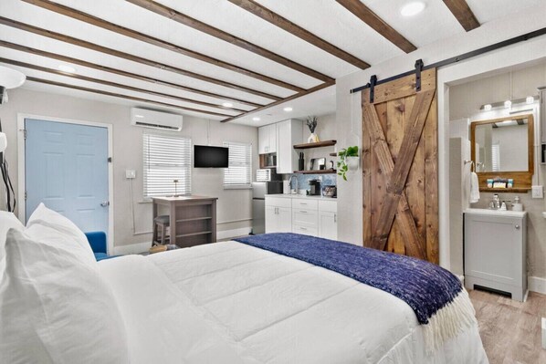 A bedroom with a bed, a desk, a TV, a kitchen area, and a bathroom. - Sala Suite 1! Monday & Thursday Fall Promo! Pet Friendly, Walk to Beach! (St. Pete Beach)