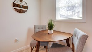 Un coin repas comprenant une table ronde en bois, deux chaises grises à revêtement rembourré, une plante en pot et une horloge murale.