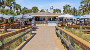 Un restaurante frente a la playa con terraza, fachada de piedra y palmeras al fondo.