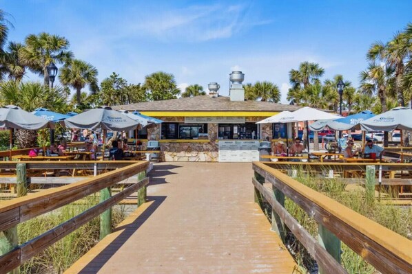 Un restaurante frente al mar con terraza, fachada de piedra y palmeras.