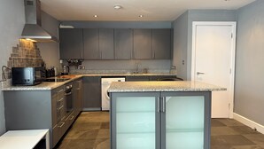 A modern kitchen with grey cabinets, a granite countertop, and a built-in dishwasher. - Heart of Buxton (Apartment) (Buxton)