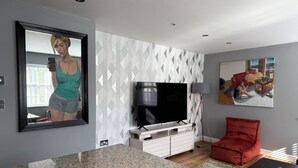 A modern living room with a flat-screen TV, a red chair, and a painting on the wall. - Heart of Buxton (Apartment) (Buxton)