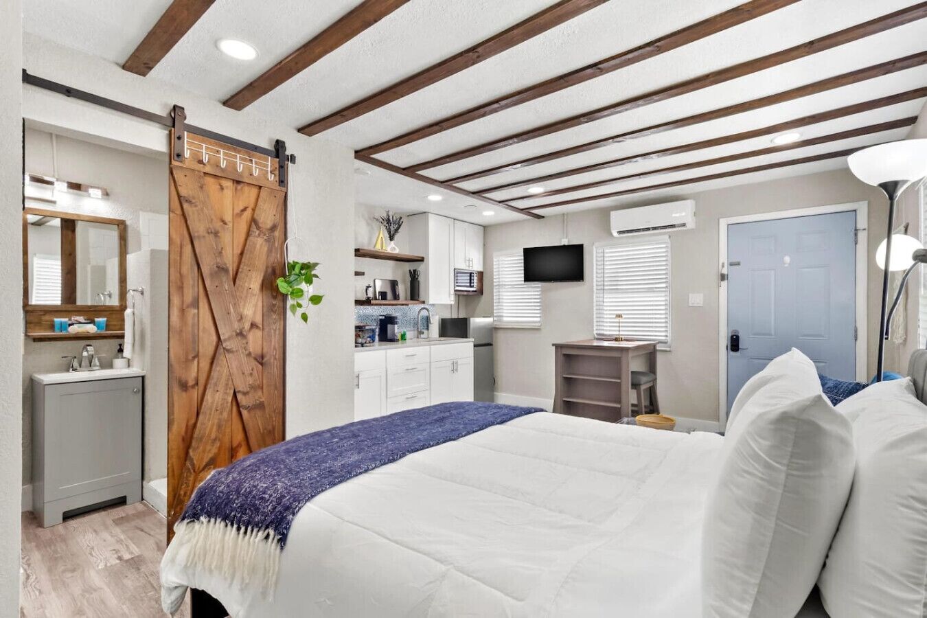 A bedroom with a bed, a wooden door, a TV, a desk, and a bathroom.
