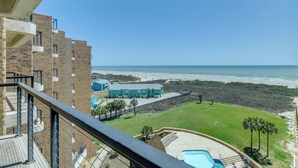 Vista de una propiedad frente a la playa con piscina, césped y un edificio con balcón con vista al océano.