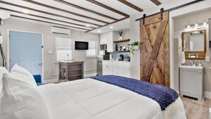 Ein Schlafzimmer mit Bett, Schreibtisch, Fernseher, Kleiderschrank und einem Badezimmer mit Spiegel und Waschbecken.