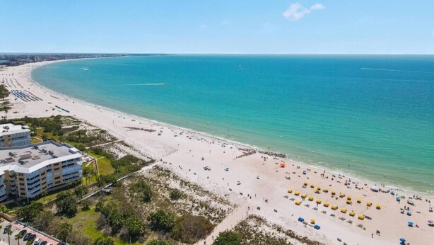 Ein Strand mit einem Hotel im Vordergrund, einem klaren blauen Meer und einem sandigen Ufer.