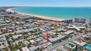 Luftaufnahme einer Küstenregion mit Strand, Hotels und einem markierten Gebäude mit rotem Pfeil.
