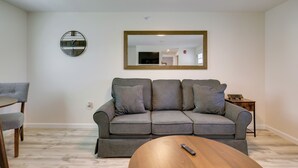 Un salon avec un canapé gris, une table basse ronde, un téléviseur et un miroir au mur.