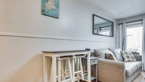 Una habitación con una consola blanca, un sofá gris, un escritorio pequeño y un espejo en la pared.