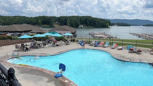 Ein Pool mit Liegestühlen und Sonnenschirmen, umgeben von einer Terrasse mit Blick auf einen See und ferne Berge.