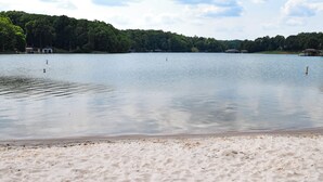 Ein sandiger Strand mit blauen Liegestühlen und einem ruhigen See.