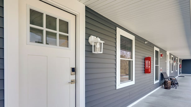 A building with a gray exterior, white trim, and a covered porch with two chairs and a trash can. - 3 Mi to Beach & Pier: Pet-Friendly Cape Cod Apt! (Wareham)