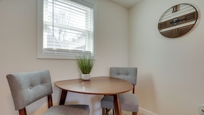 A dining area with a round wooden table, two upholstered chairs, a potted plant, and a wall clock. - 3 Mi to Beach & Pier: Pet-Friendly Cape Cod Apt! (Wareham)